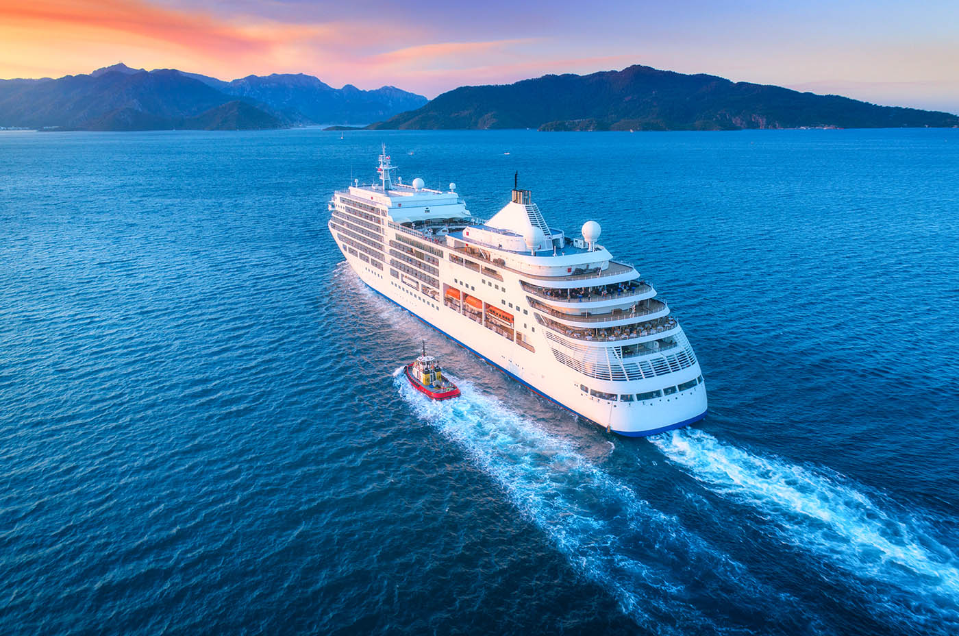 Cruise ship at harbor. Aerial view of beautiful large white ship at sunset. Colorful landscape with boats in marina bay, sea, colorful sky. Top view from drone of yacht. Luxury cruise. Floating liner